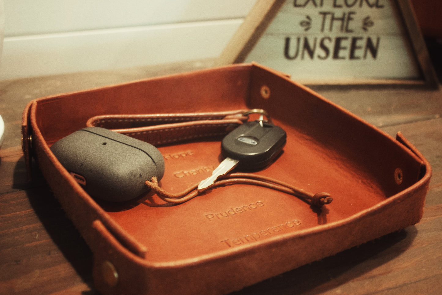 keychain and airpods on a leather valet tray with the theological and cardinal virtues stamped