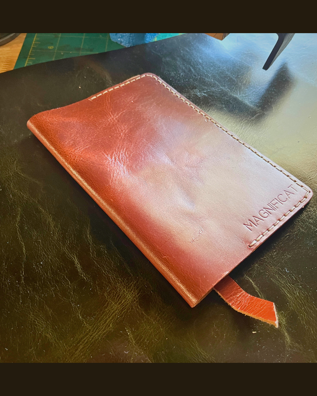 Brown leather wallet on a dark surface with 'MAGNIFICAT' branding.