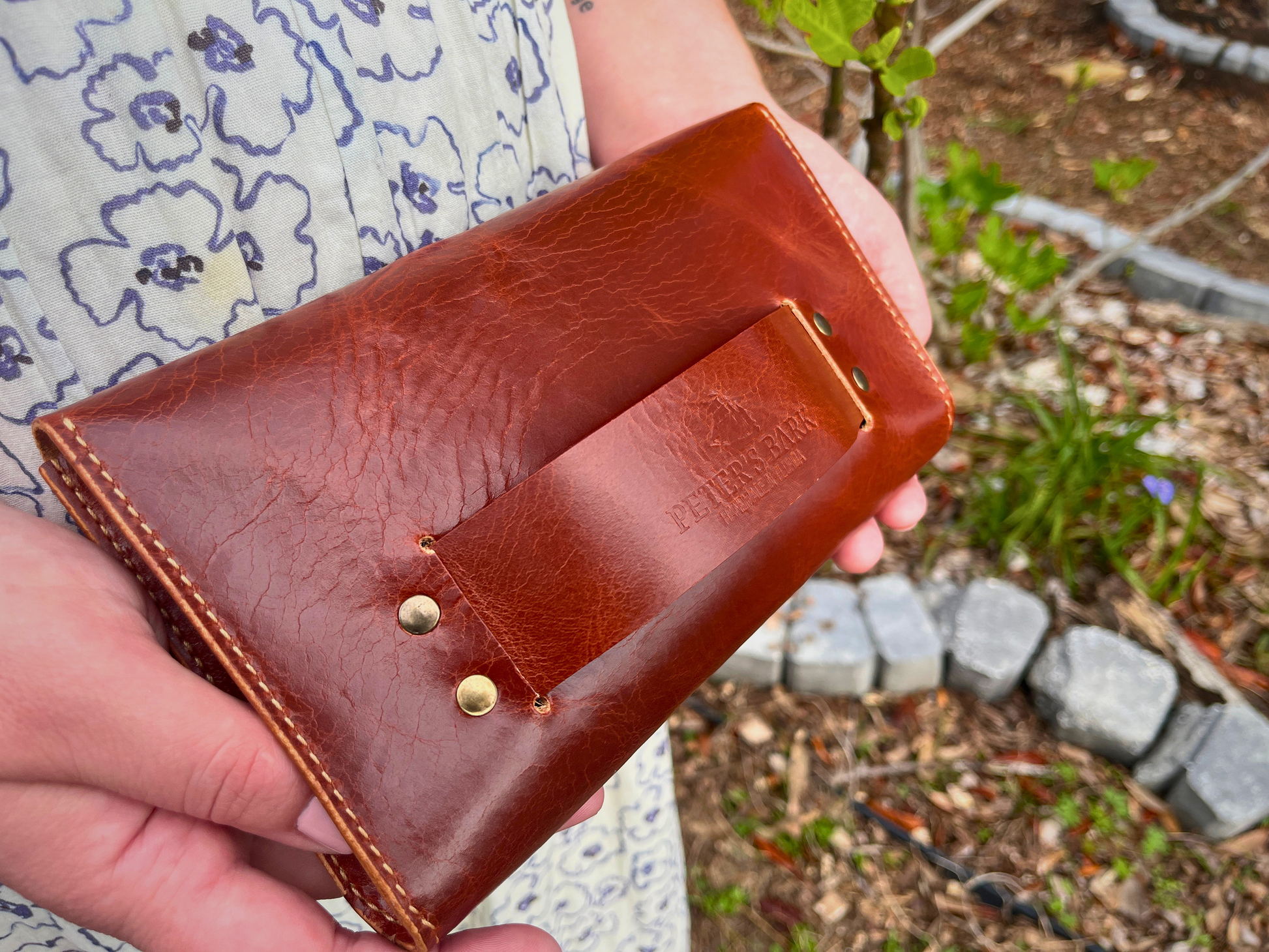 Brown leather clutch bag held by a person with a blurred outdoor background