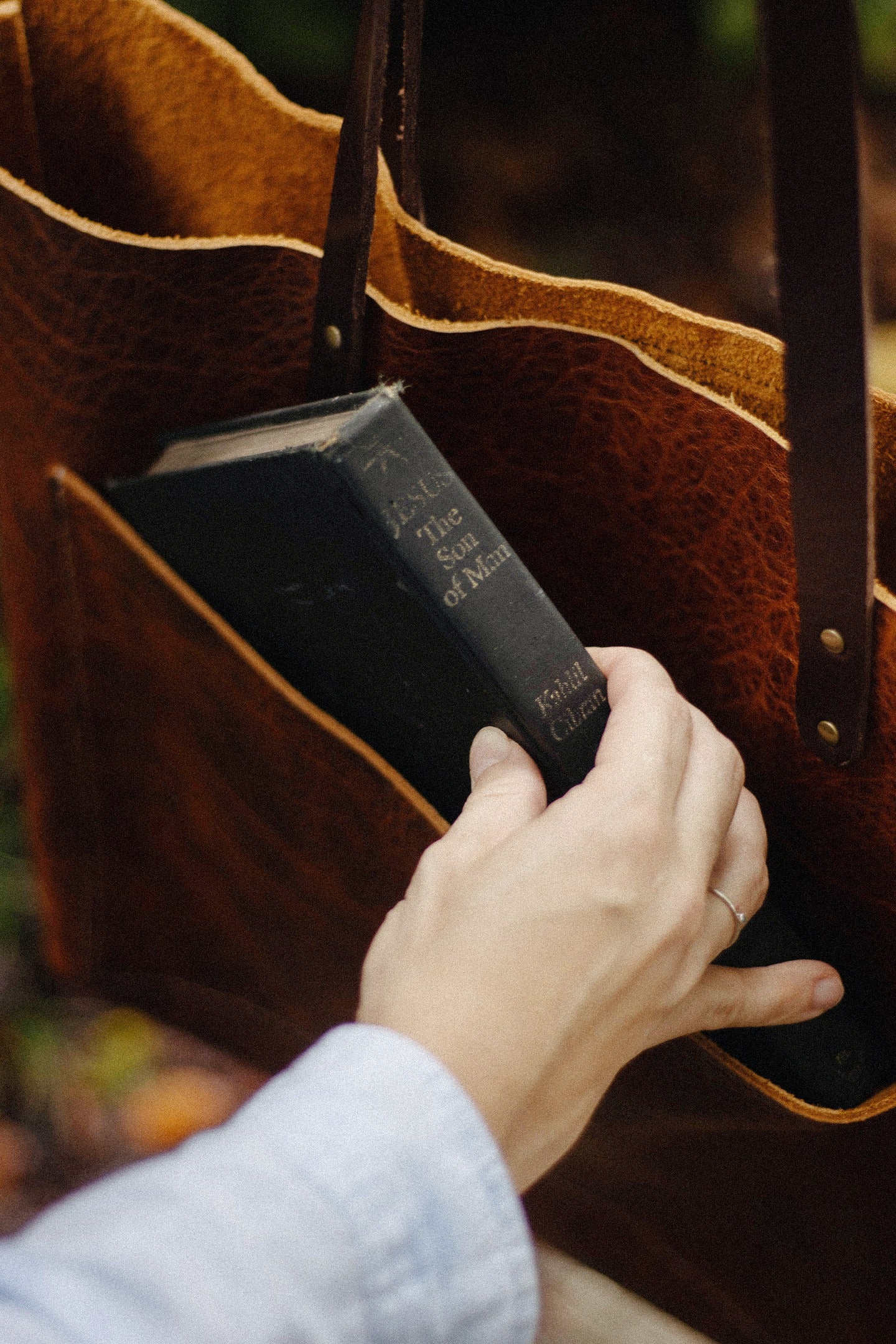 Hand placing a black book into a brown leather bag.