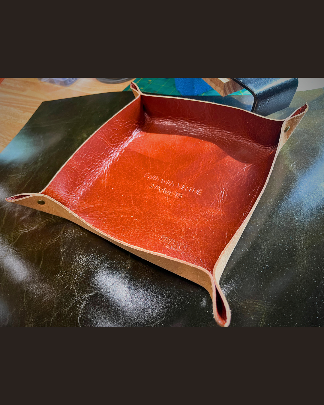 Light brown leather tray with visible branding on a dark surface