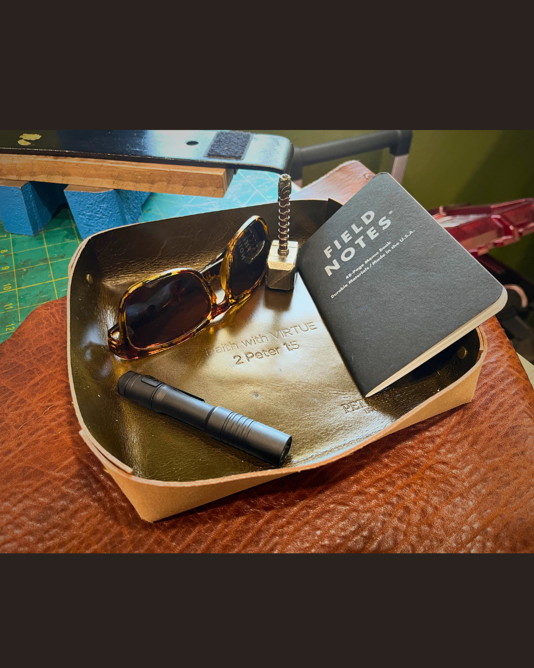 Sunglasses, field notes, and a flashlight on a wooden stand with a green surface underneath.